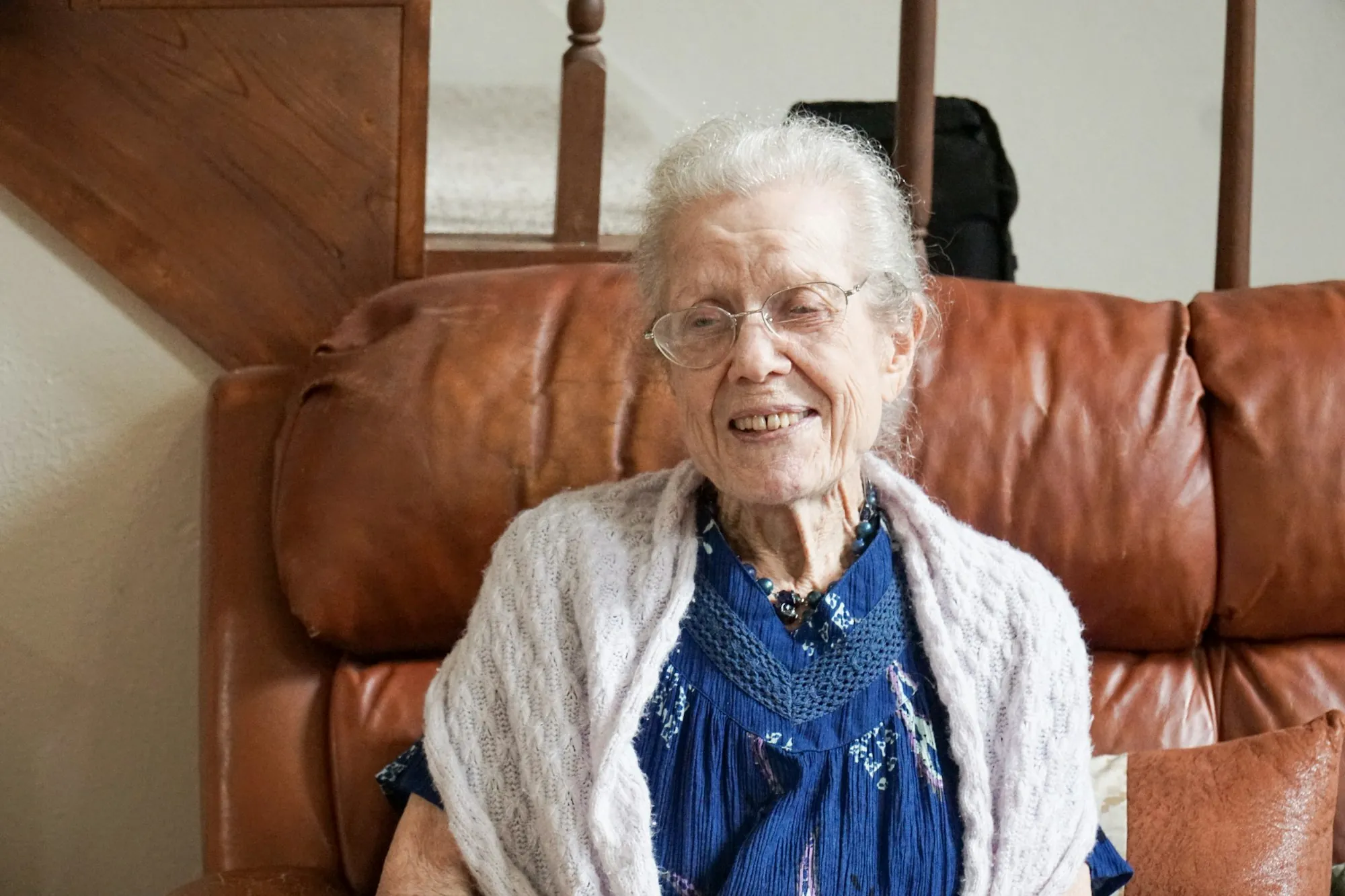 An older woman in a cardigan sitting on a sofa at home