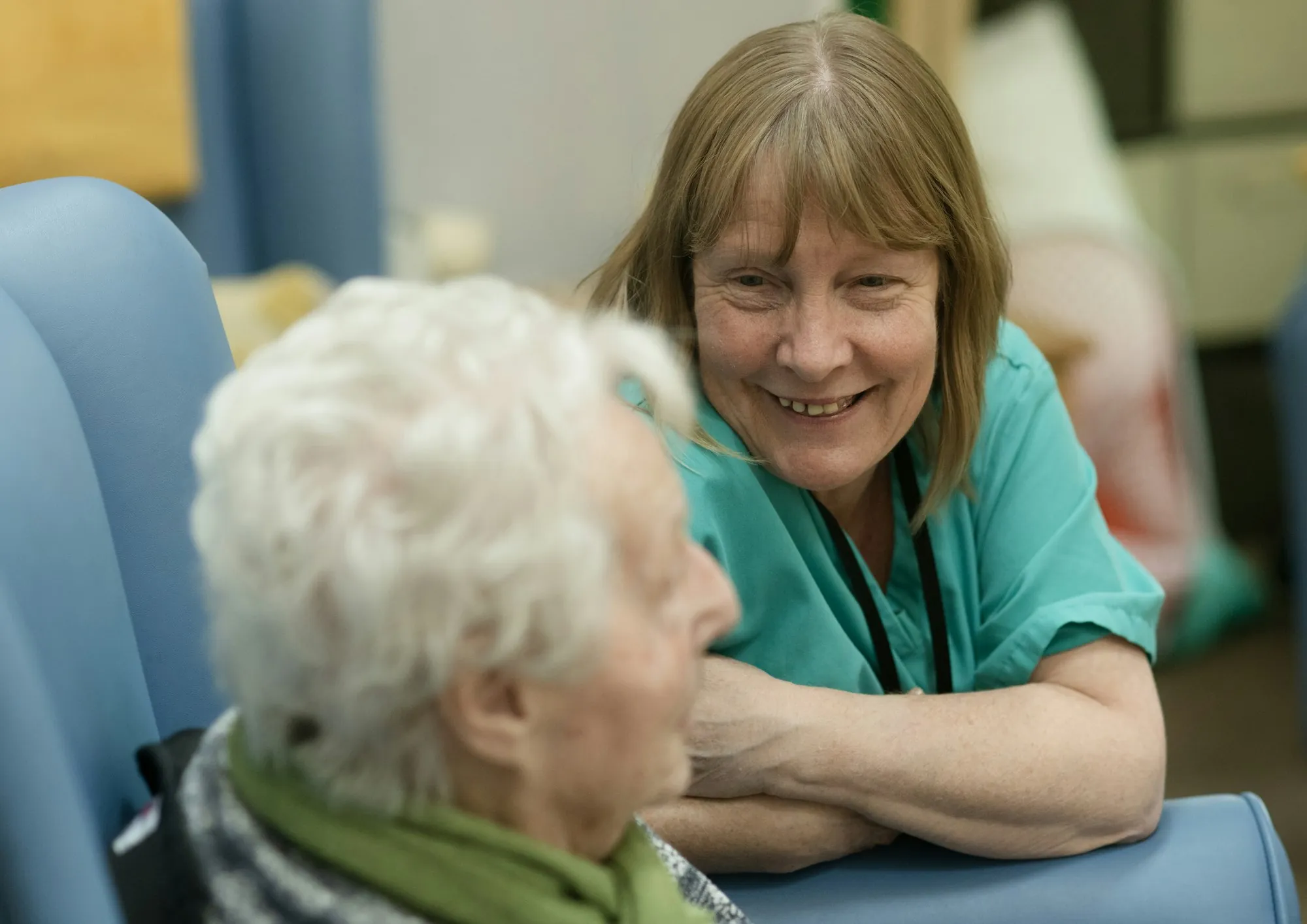 A care worker leaning in to talk with an older woman in her armchair