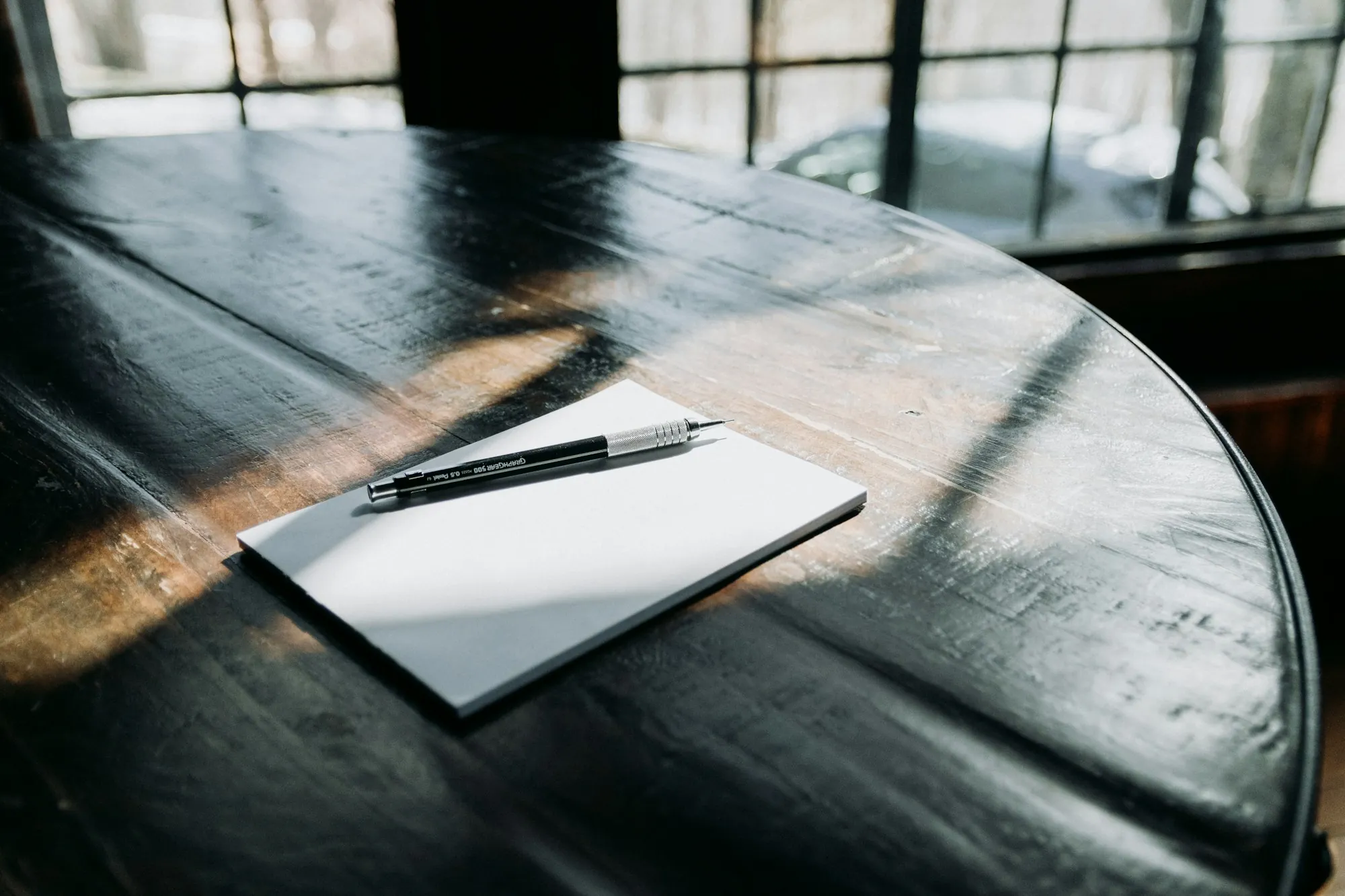 An open notebook with a pen and pencils on a desk