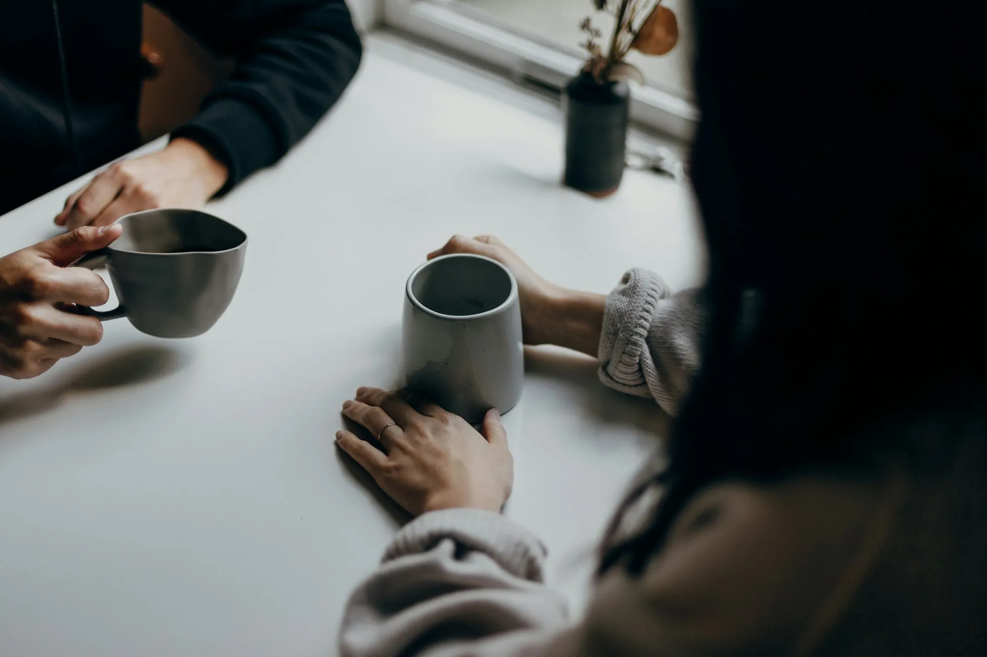 Two people sitting at a table holding mugs, mid-conversation